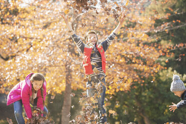 Verspielte Jungen und Mädchen laufen und springen im Herbstlaub - HOXF00654