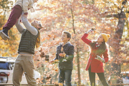 Verspielter Vater und Kinder spielen im Herbstlaub - HOXF00656