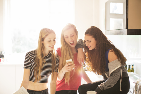 Teenager-Mädchen, die mit ihrem Handy in der sonnigen Küche SMS schreiben, lizenzfreies Stockfoto