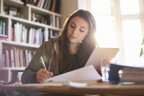 Teenage girl with digital tablet doing homework at desk stock photo