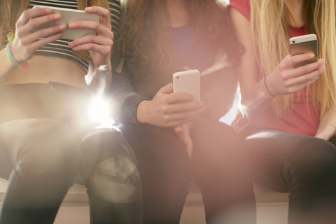 Teenage girls texting with cell phones in a row stock photo