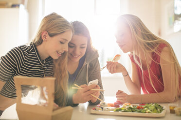 Teenager-Mädchen essen Sushi und simsen mit Handy in der sonnigen Küche - HOXF00717