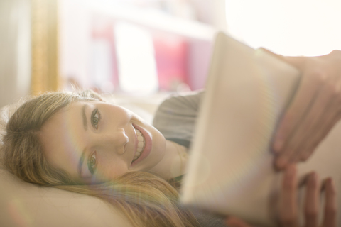 Portrait lächelndes Teenager-Mädchen mit digitalem Tablet auf dem Bett, lizenzfreies Stockfoto