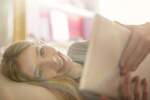 Portrait lächelndes Teenager-Mädchen mit digitalem Tablet auf dem Bett - HOXF00720