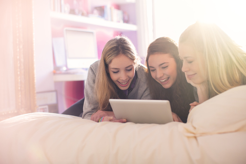 Teenager-Mädchen mit digitalem Tablet auf dem Bett im sonnigen Schlafzimmer, lizenzfreies Stockfoto