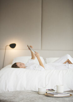 Frau im Bademantel auf dem Bett liegend mit digitalem Tablet - HOXF00736