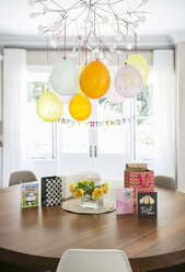 Smiley-Luftballons und Happy-Birthday-Schild hängen über Tisch mit Karten - HOXF00749