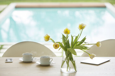 Gelber Tulpenstrauß und Kaffeetassen auf einem Tisch am Pool - HOXF00779