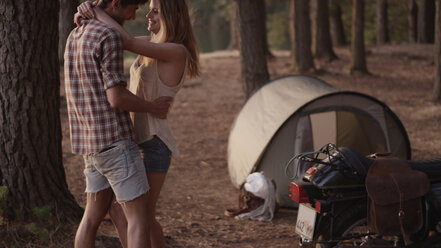 Affectionate young couple hugging outside tent in woods - HOXF00781