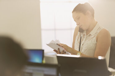 Geschäftsfrau, die telefoniert und Papierkram im Büro durchgeht - HOXF00868