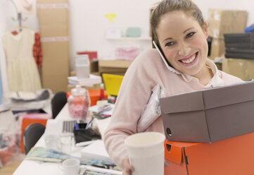 Lächelnde Modeeinkäuferin beim Multitasking im Büro - HOXF00877