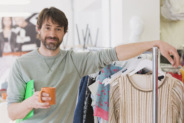 Portrait confident male fashion buyer drinking coffee leaning on rack - HOXF00881