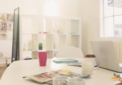 Laptop, Kaffeetassen und Modezeitschriften auf dem Tisch im Büro - HOXF00899