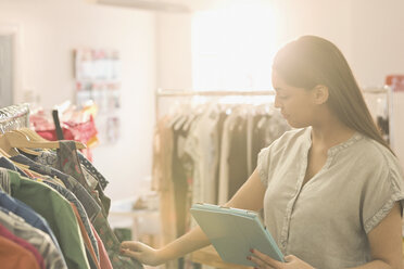 Fashion buyer with digital tablet browsing clothing on rack - HOXF00910