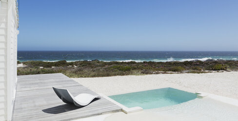 Pool und moderner Liegestuhl mit Blick auf das Meer unter sonnigem, blauem Himmel - HOXF00946