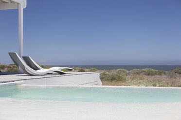 Swimmingpool und moderne Liegestühle mit Blick auf den Ozean unter sonnigem, blauem Himmel - HOXF00963