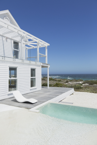 Weißes Strandhaus und Swimmingpool mit Blick auf das Meer unter sonnigem blauem Himmel, lizenzfreies Stockfoto