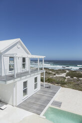 Weißes Strandhaus und Swimmingpool mit Blick auf das Meer unter sonnigem blauem Himmel - HOXF00980