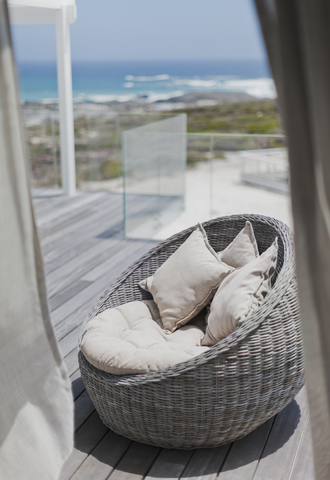 Korbstuhl mit Kissen auf der sonnigen Terrasse des Strandhauses mit Meerblick, lizenzfreies Stockfoto