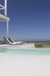 Moderne Liegestühle am Pool mit Blick auf das Meer unter sonnigem blauem Himmel - HOXF00991