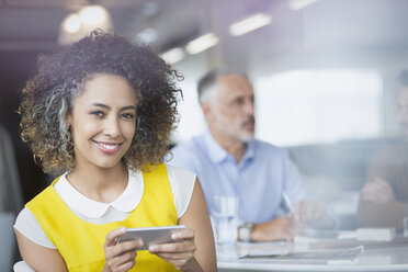 Porträt einer lächelnden Geschäftsfrau, die in einer Besprechung eine SMS mit ihrem Mobiltelefon schreibt - HOXF01004