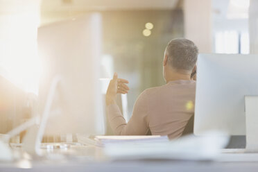 Geschäftsmann gestikuliert am Schreibtisch in einem sonnigen Büro - HOXF01008