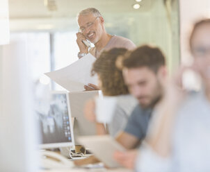 Architekt mit Bauplänen, der in einem Büro telefoniert - HOXF01016