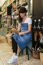 Frau sitzt auf einem Hocker in einem Geschäft und macht sich Notizen - EBSF02195