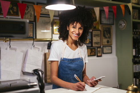 Porträt einer lächelnden Frau mit Handy und Notizbuch in einem Geschäft - EBSF02208