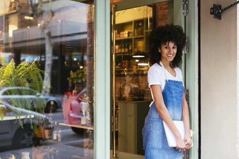 Porträt einer lächelnden Frau, die in der Eingangstür eines Geschäfts steht - EBSF02235