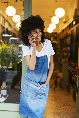 Glückliche Frau mit Mobiltelefon in der Eingangstür eines Geschäfts, lizenzfreies Stockfoto