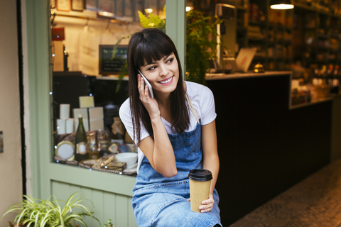 Smiling woman sitting at entrance door of a store talking on cell phone stock photo