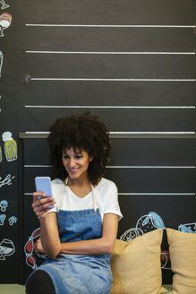 Lächelnde Frau sitzt auf einer Bank in einem Geschäft und benutzt ein Mobiltelefon - EBSF02252