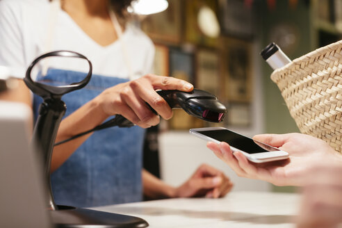Nahaufnahme eines Kunden, der bargeldlos mit seinem Smartphone an der Kasse eines Geschäfts bezahlt - EBSF02259