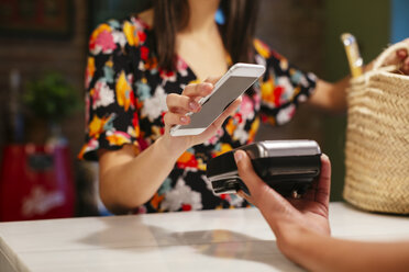 Nahaufnahme eines Kunden, der bargeldlos mit seinem Smartphone an der Kasse eines Geschäfts bezahlt - EBSF02262