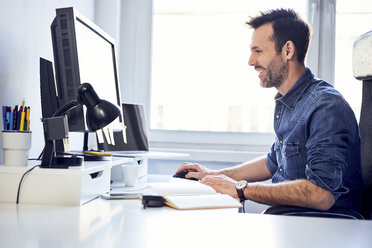 Lächelnder Mann arbeitet am Computer am Schreibtisch im Büro - BSZF00236