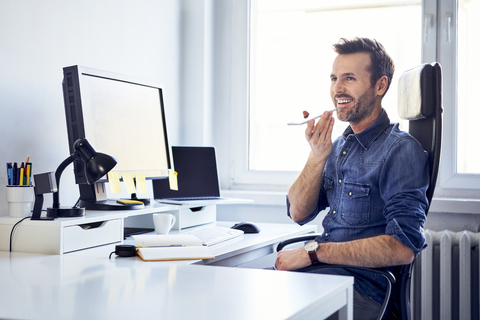 Lächelnder Mann mit Smartphone am Schreibtisch im Büro, lizenzfreies Stockfoto