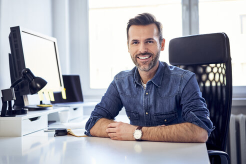 Porträt eines lächelnden Mannes, der am Schreibtisch im Büro sitzt - BSZF00239