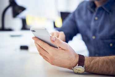 Nahaufnahme eines Mannes, der ein Mobiltelefon am Schreibtisch im Büro benutzt - BSZF00241