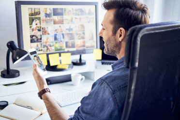 Fotoredakteur am Schreibtisch im Büro mit Videochat auf seinem Telefon - BSZF00242