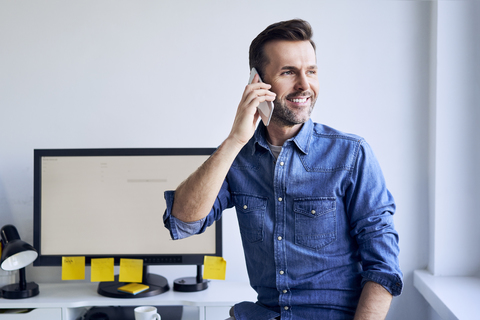 Lächelnder Mann am Schreibtisch im Büro beim Telefonieren, lizenzfreies Stockfoto