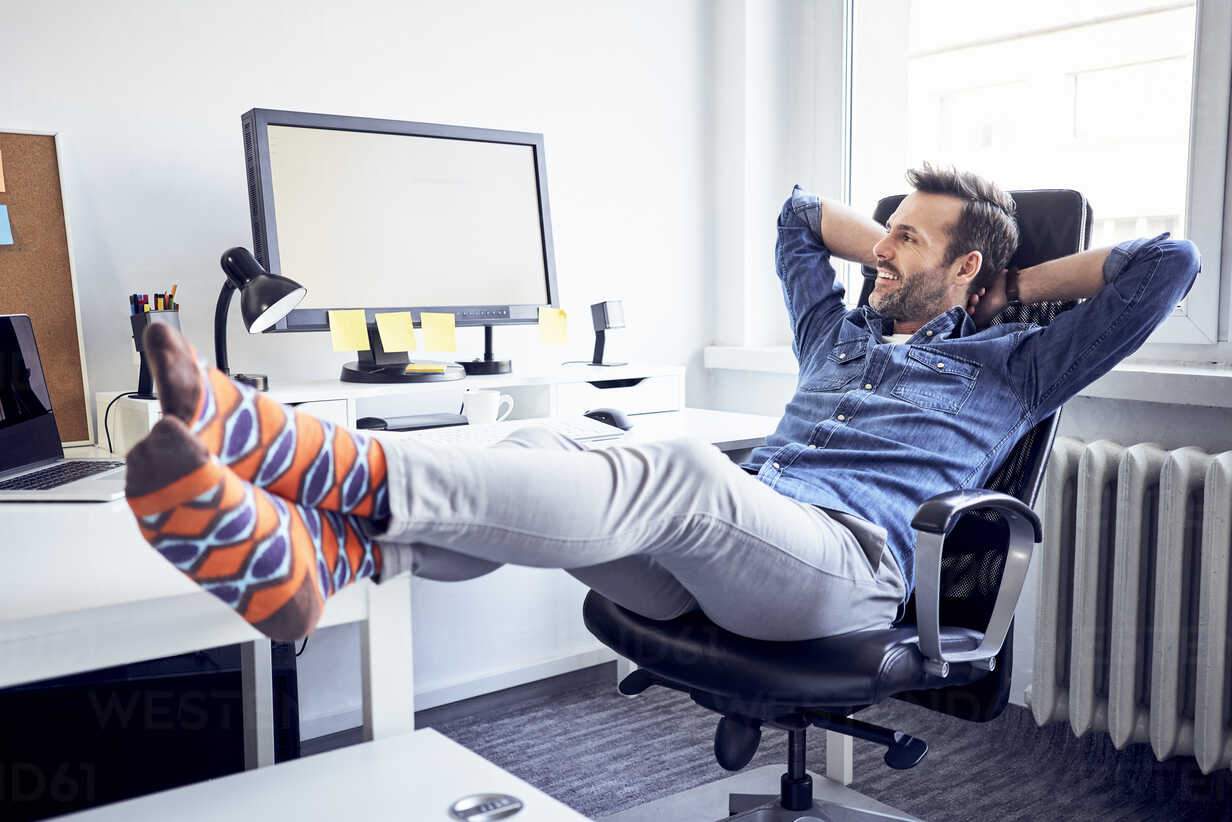 Relaxed man sitting at desk in office looking at computer screen