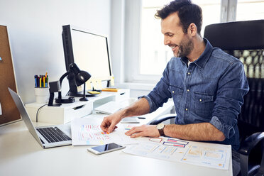 Smiling web designer working on draft at desk in office - BSZF00262