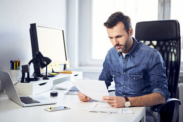 Man reading document at desk in office - BSZF00265