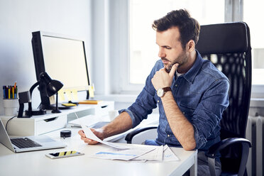 Man reading document at desk in office - BSZF00266