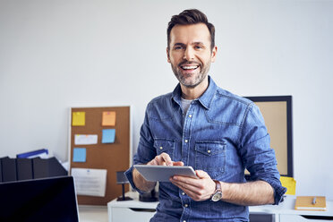 Porträt eines lächelnden Mannes, der ein Tablet im Büro benutzt - BSZF00273