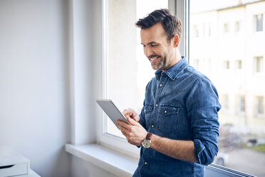 Lächelnder Mann mit Tablet am Fenster - BSZF00277