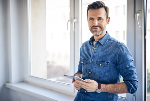 Porträt eines lächelnden Mannes, der eine Tafel am Fenster hält, lizenzfreies Stockfoto