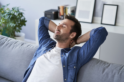 Lächelnder, entspannter Mann, der auf dem Sofa sitzt und träumt, lizenzfreies Stockfoto