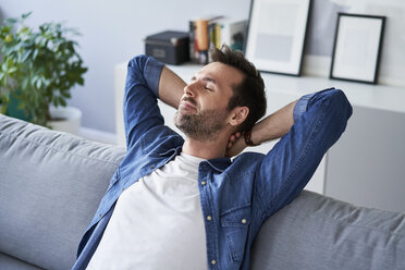 Smiling relaxed man sitting on sofa daydreaming - BSZF00287